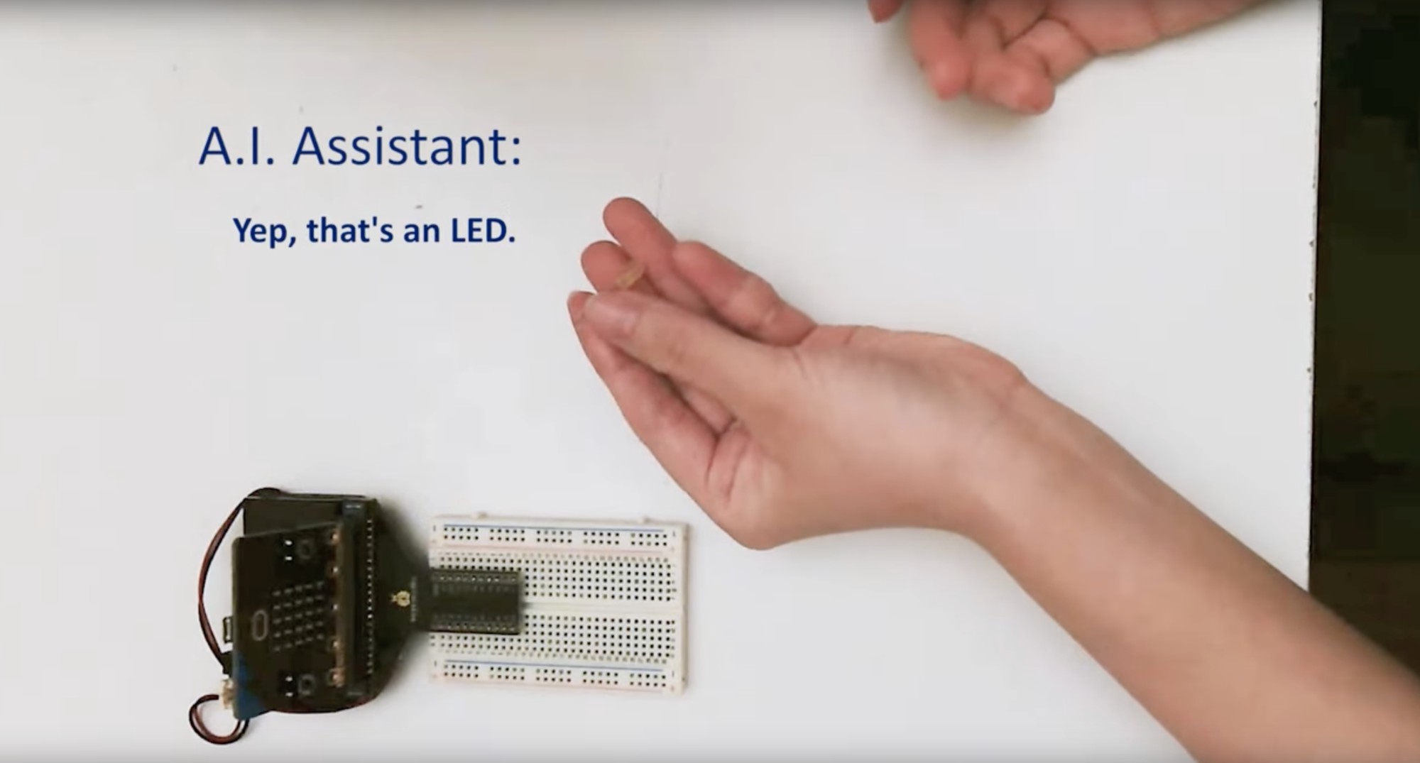 A breadboard, an LED held in one of two hands, and text that reads A.I. Assistant: Yep, that's an LED